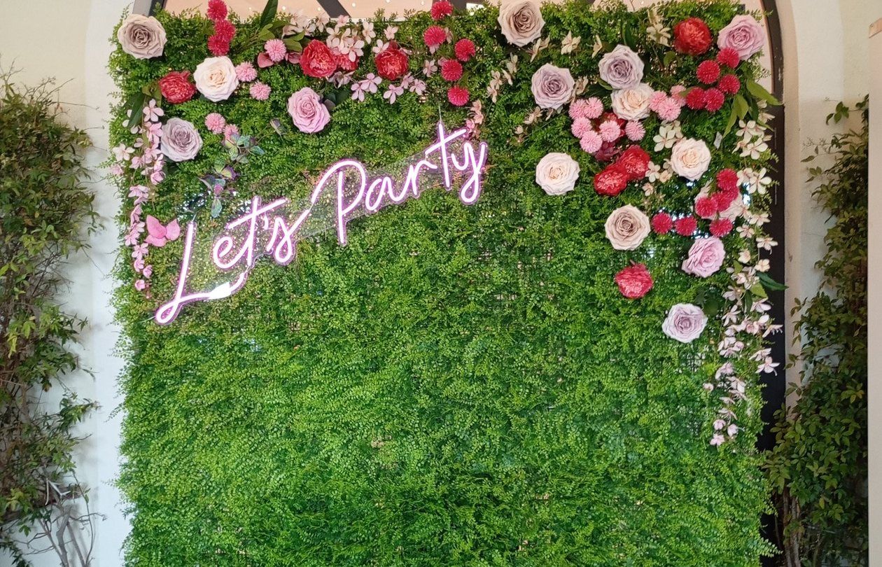 Parete verde con fiori e scritta al neon Let's Party